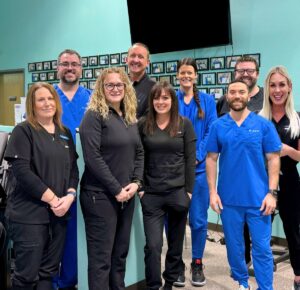 Team of nurses standing with chiropractors and office managers behind them. Everyone looks and smiles directly at the camera. This team can administer medications like GLP-1 near Iowa City to help patients feel less joint pain.