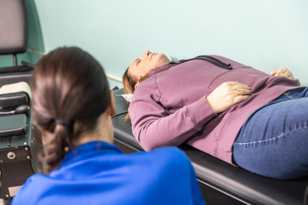 Patient lays on top of a a spinal decompression device as part of a routine chiropractic service that addresses how to reduce inflammation in the spine. This system gently stretches the spine to relieve pressure on her spinal discs and joints. Show less