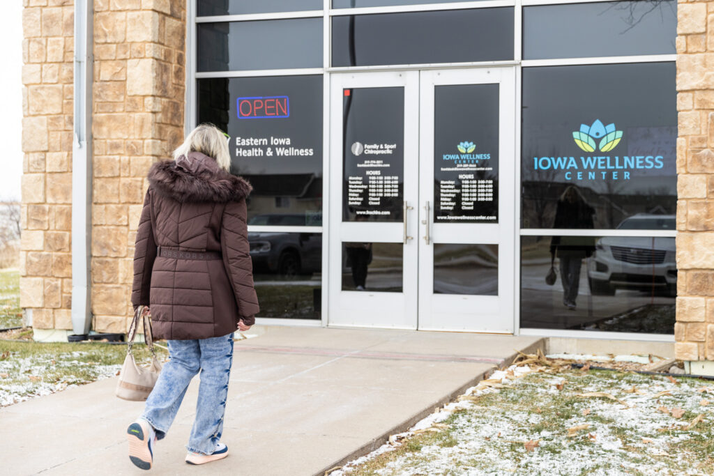 Woman wearing a big coat walk towards the entrance of a chiropractic office to receive treatments for neck pain relief near Iowa City