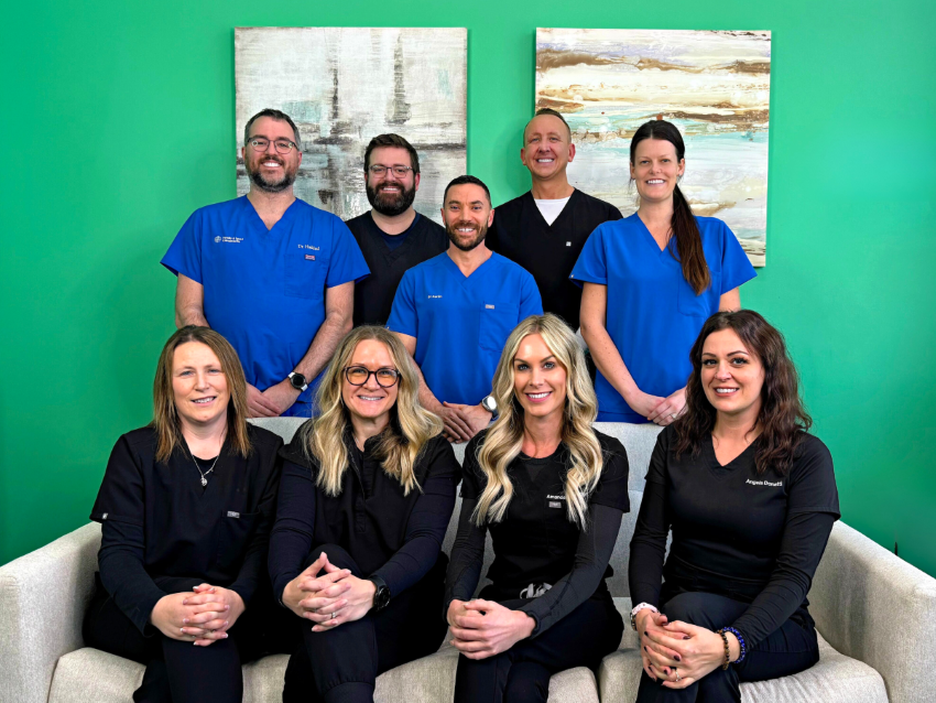 Team of nurses sitting on a couch with chiropractors and office managers standing behind them. Everyone looks and smiles directly at the camera. This team can administer medications like GLP-1 near Iowa City to help patients feel less joint pain.