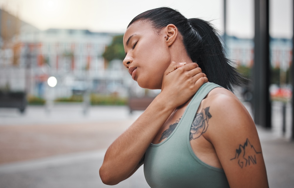 Woman holds neck while standing outside because she feels a strain and needs to seek neck pain treatment near Cedar Rapids
