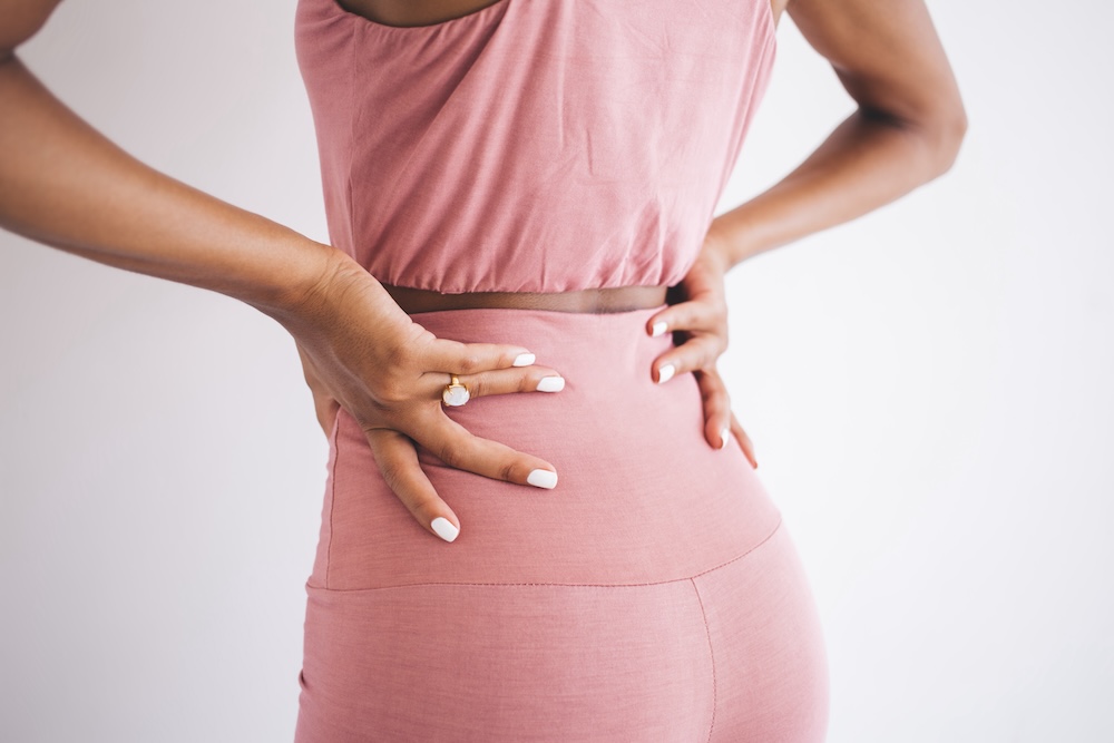 Woman places hands on lower back and tries to alleviate pain radiating up her spine. She's about to go to a physical therapist to find back strain relief in North Liberty.