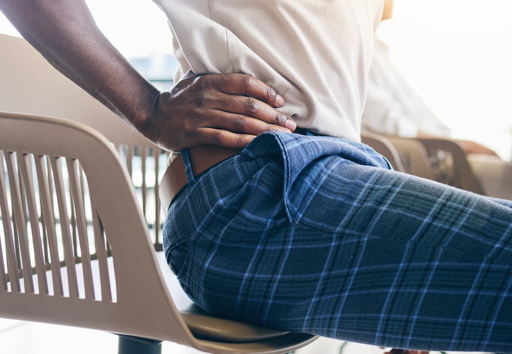 Person adjusts themselves in seat with a hand located on the source of their aching. This is a sign that they need hip pain treatment near Cedar Rapids.